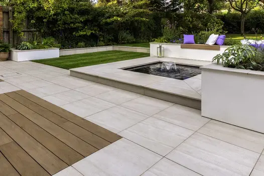Faro porcelain patio slabs laid with composite decking edge square pond and lawn. Built by Brockstone Landscape Construction.