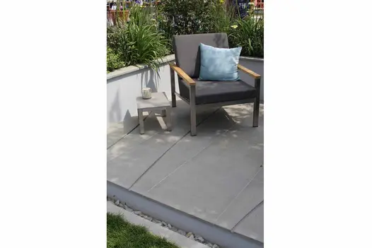 Chair sits in corner of right-angled raised bed, on Flamed Grey sawn sandstone paving with curved grooves cut across it.