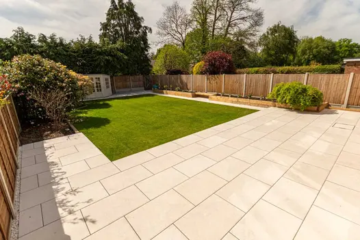 Fenced garden with summerhouse on far side of square lawn in front of deep patio of Florence Beige Porcelain outdoor tiles. 