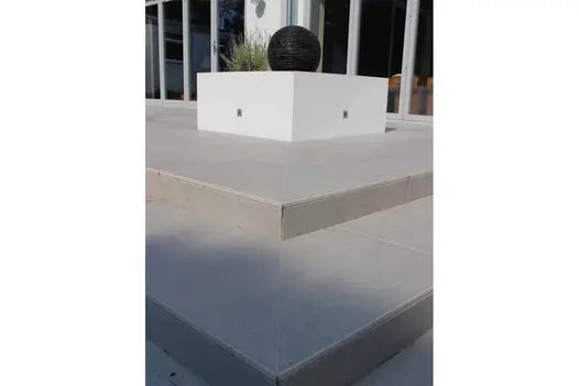 Close view of mitred corners of 2 shallow Florence Grey porcelain steps and risers up to matching patio. Design by Neil Jones.
