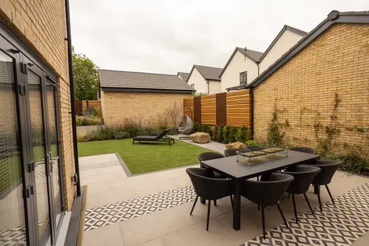 Platinum Grey Porcelain planks create edge between lawn and patio in garden with outdoor dining set. Built by BRP Garden Services.
