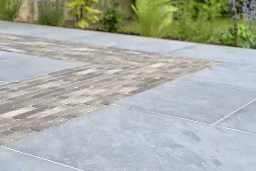 Close view of grey Florence Storm porcelain paving with inset strip clay paver detailing. Design by Bark Brick Block.