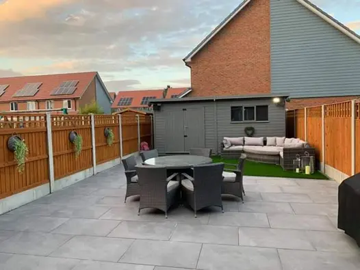 Fenced garden fully paved in Florence Storm Porcelain outdoor tiles UK, with shed at end and 2 sets of dining and lounge furniture.