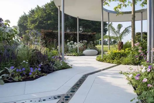 Bespoke-cut Florence White porcelain slabs pave show garden. Modern metal grille covers rill leading to central round flower bed.