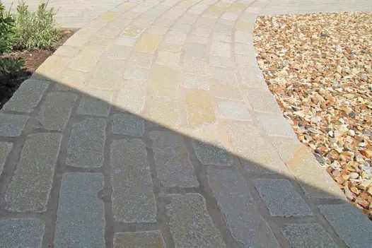 Flowpoint Natural Grey used as jointing mortar for cobbled paving curving alongside decorative gravel.