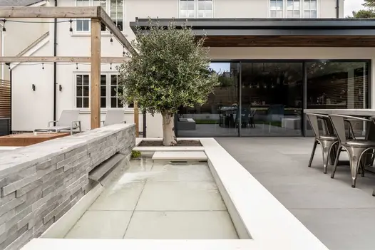 Stone clad water feature with a stainless steel rill spilling over into a shallow pool faced in Sidewalk porcelain slabs.