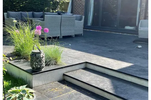 2 steps descend from Midnight Black limestone paving patio with large rattan dining set outside dark grey bifold doors.