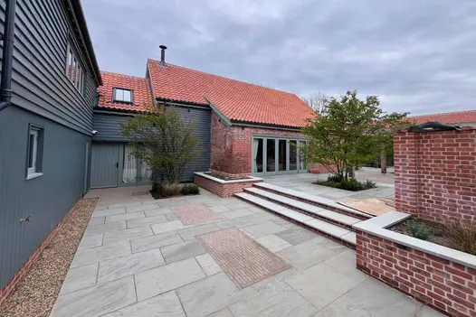 Multi level kandla grey indian sandstone patio with clays inset in unique pattern has steps leading to upper level.