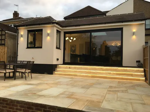 3 steps with undertread lighting descend from modern extension with wide sliding doors to Mint Indian sandstone patio.