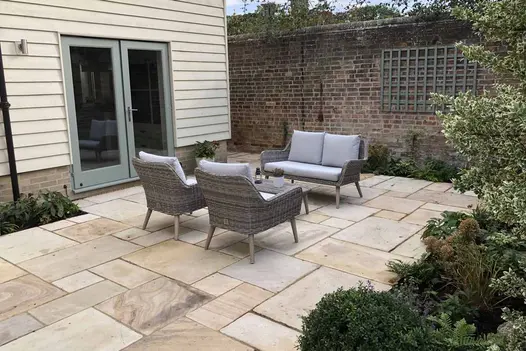 Mint sandstone paving shows off its unique fossils and colours with grey rattan furniture in the middle.