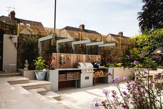 Jura beige smooth limestone bullnose steps leading down to outdoor kitchen with wood burner and BBQ, dining area in the background.