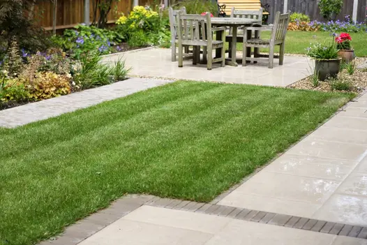 Small lawn surrounded by Porcelain and Clay paving and a centrally situated wooden garden table and chairs.