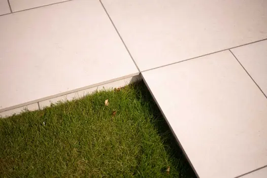 Right-angled corner of grass, edged by raised Florence Beige Porcelain patio slabs with dark grey joints. Built by Garden Tamer.