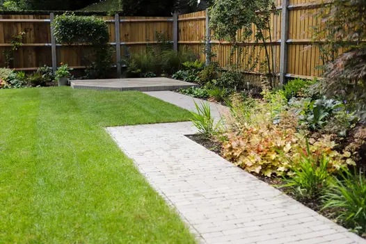Straight-edged path of Stone Grey clay pavers, with 2 right-angled bends, leads between planted beds and lawn to raised patio.