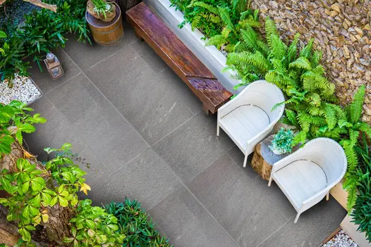Looking down into a walled garden planted with ferns in raised beds and a pair of wicker seats on top of a porcelain patio.