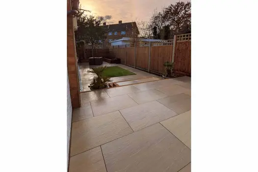 Long narrow fenced plot with wet patio of Raj Green porcelain garden tiles UK and 2 steps down to lawn framed by path. 