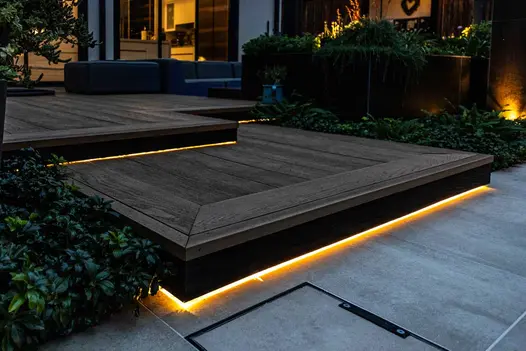 Close up of corner of golden oak millboard decking step with profiled edge and darker shade fascias with lights underneath.