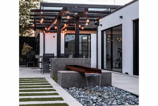 Vulcano Ceniza Designclad faces rectangular raised bed with topiary balls in front of matching wall with metal circles hung on it. 
