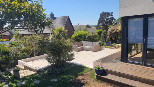 Living-room leading to decking area with Millboard composite decking, followed by a seating area paved with Gea Porcelain Paving.