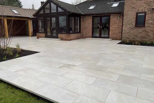 Gea Porcelain Downstand Steps used on a large patio with pale paving and brick exterior.