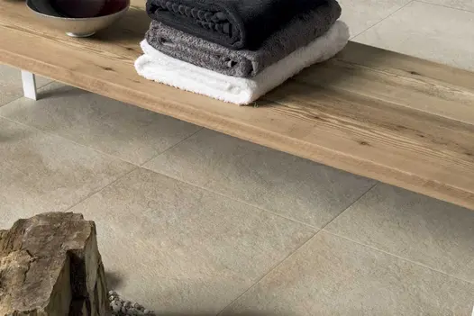 Close image of an outdoor relaxation area featuring Gea vitrified porcelain paving and a wooden garden bench with towels.