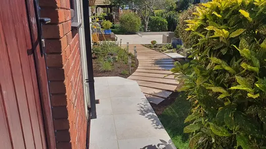 Gea Porcelain Paving garden path leading to a larger paved area that also features soft-landscaping and garden furniture.