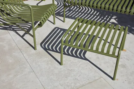 Green slatted metal armchair and table cast shadows onto Jura Grey smooth limestone paving slabs with narrow joints.