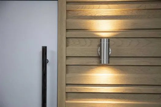 Golden Oak Board & Batten cladding installed around a front door, paired with brushed steel wall lighting.