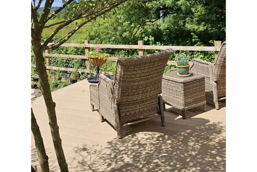 Countryside views from rattan armchair sitting on golden oak millboard decking with trees casting shadows on the garden furniture.