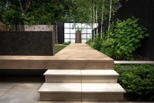 2 steps up to Golden Oak Millboard decking path between lawn and border in Japanese style garden designed by Robert Hughes.