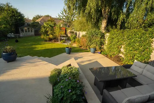 Terrace in Golden Stone Porcelain with inset flower bed and steps descending to lawn-level patio with modular outdoor furniture.