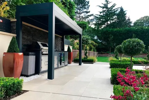 Golden Stone Porcelain patio, with linear outdoor kitchen under metal pergola and formal beds with clipped hedging and topiary.