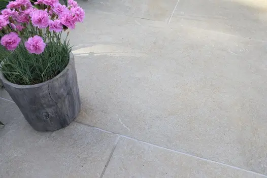 A round planter growing carnations stands on Golden Stone Porcelain paving in running bond pattern, pointed with Norcros grout.