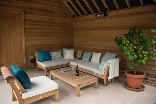 Interior corner of wooden roofed shelter, with wooden sofa, table and chair, paved with Golden Stone Porcelain pavers.