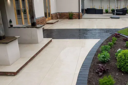 Golden Stone Porcelain along with Midnight black limestone setts to edge, curved around a flowerbed with steps leading to house.
