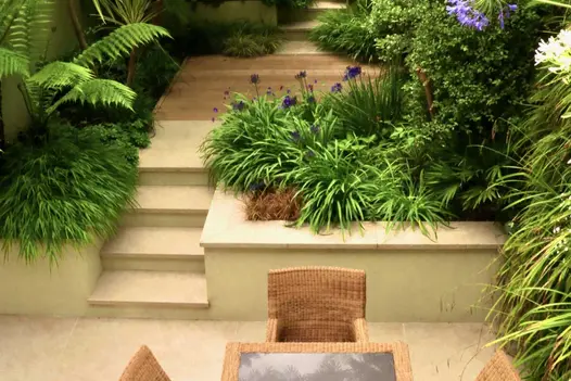Golden Stone porcelain wall coping tops retaining walls of terrace punctuated by 4 narrow steps rising from paving to decked area.