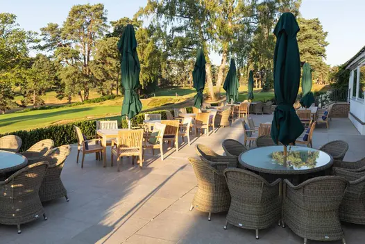 Golf club terrace with wicker and wood furniture, laid with acid washed limestone paving in warm sunlight.