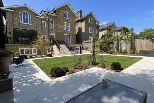 L-shaped lawn beneath large villa is surrounded by wide path of Florence White porcelain paving. Mug on table in foreground.