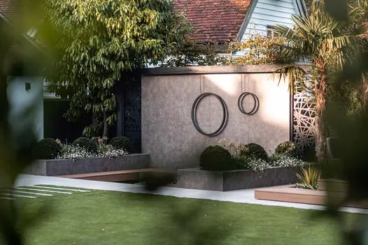 Two rings hang on a feature wall in the distance and a raised flowerbed, both clad in Vulcano Ceniza porcelain cladding.