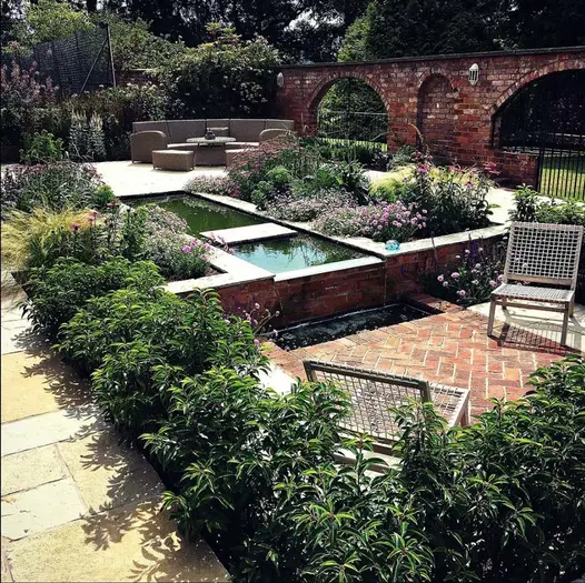 Water feature in the middle of garden runs to waterfall that flows into Dorset Antique Clay Pavers with planting surrounding.