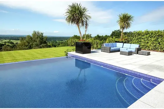 Curved steps descend into water in corner of blue infinity pool with view over countryside from Silver Grey granite patio.