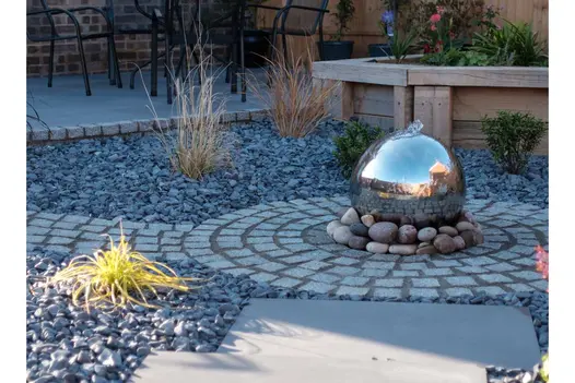 Bubbling ball water feature on cobbles in centre of Silver Grey granite sett circle. Grasses planted in surrounding gravel.