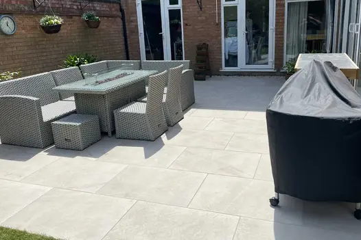 Multiple patio doors opening out onto a large porcelain patio with 8 seater Rattan dining set and covered up barbecue.