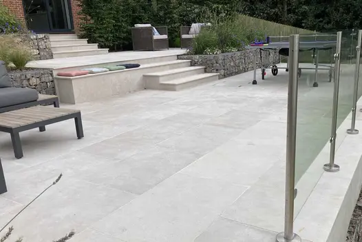 Terraced levels of Egyptian beige limestone paving descend from house via matching steps, with raised beds of stone-filled gabions.