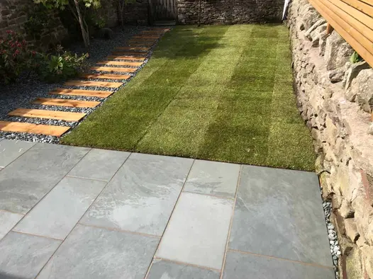 Rectangular lawn edged on 2 sides by path of planks set in gravel and patio of Brazilian Grey slate paving. Built by Green Bear.