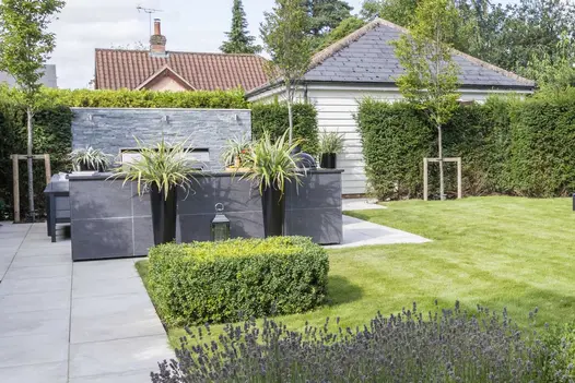 3 downlighters set at top of wall of Green slate external cladding, partially hidden behind bar and planters on paving next to lawn.