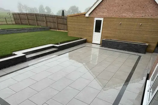 Wet patio has water trough feature, steps rising to lawn and another wall on raised area clad in green slate external cladding.