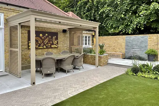 Water cascades into rectangular pond from spout in wall with Green slate cladding on boundary of garden with lawn and topiary.
