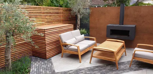 Slatted fence and storage box behind lounge set on grey paving inset with Silver Grey Multi clay paving. By Greenbird Gardening.