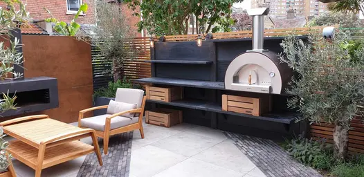Black shelving with pizza oven sits on porcelain paving inset with Silver Grey Multi brick pavers. Design by Greenbird Gardening.